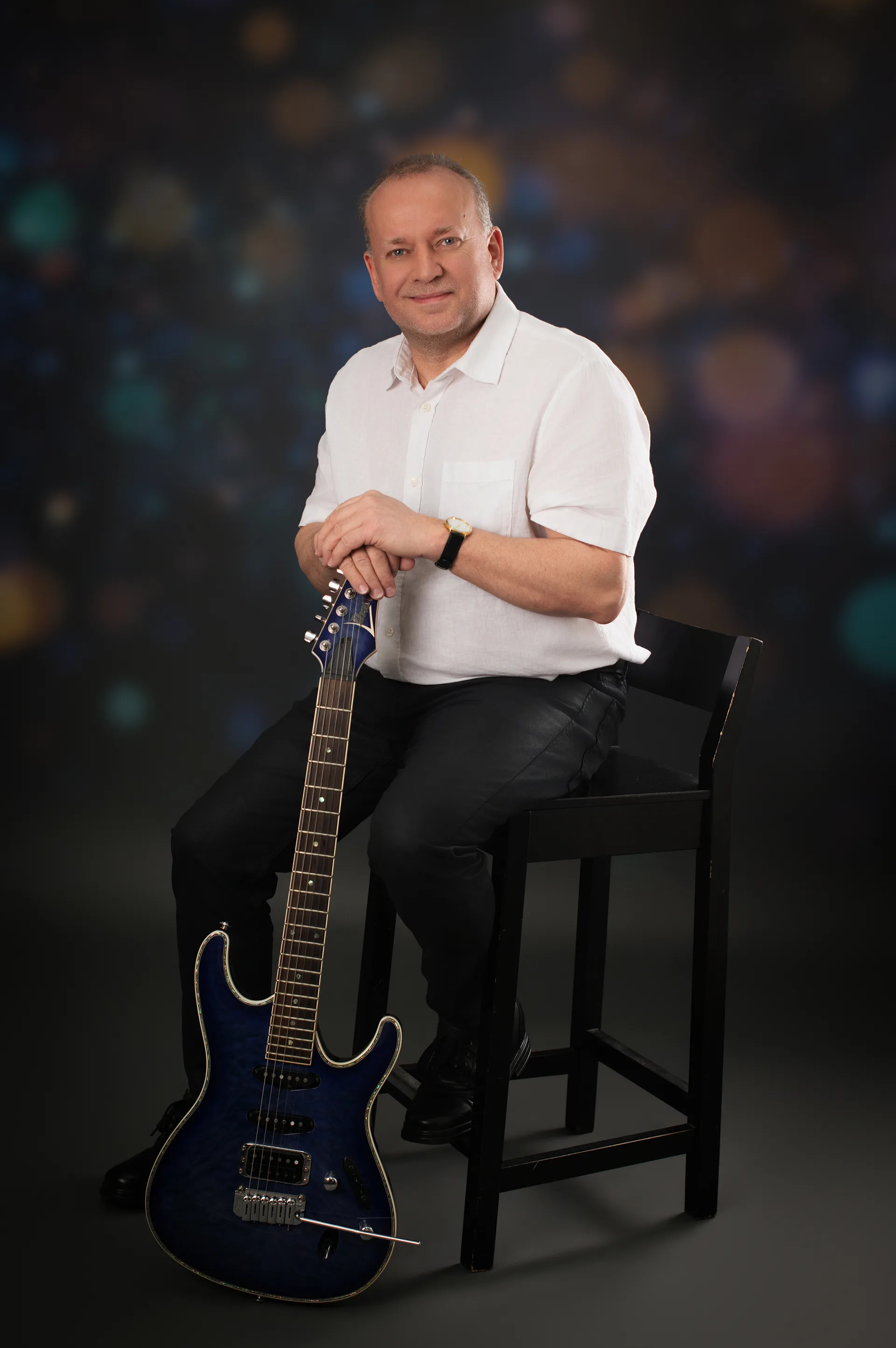 Gerald Stefan Allmann sitzend mit E-Gitarre vor Bokeh-Hintergrund