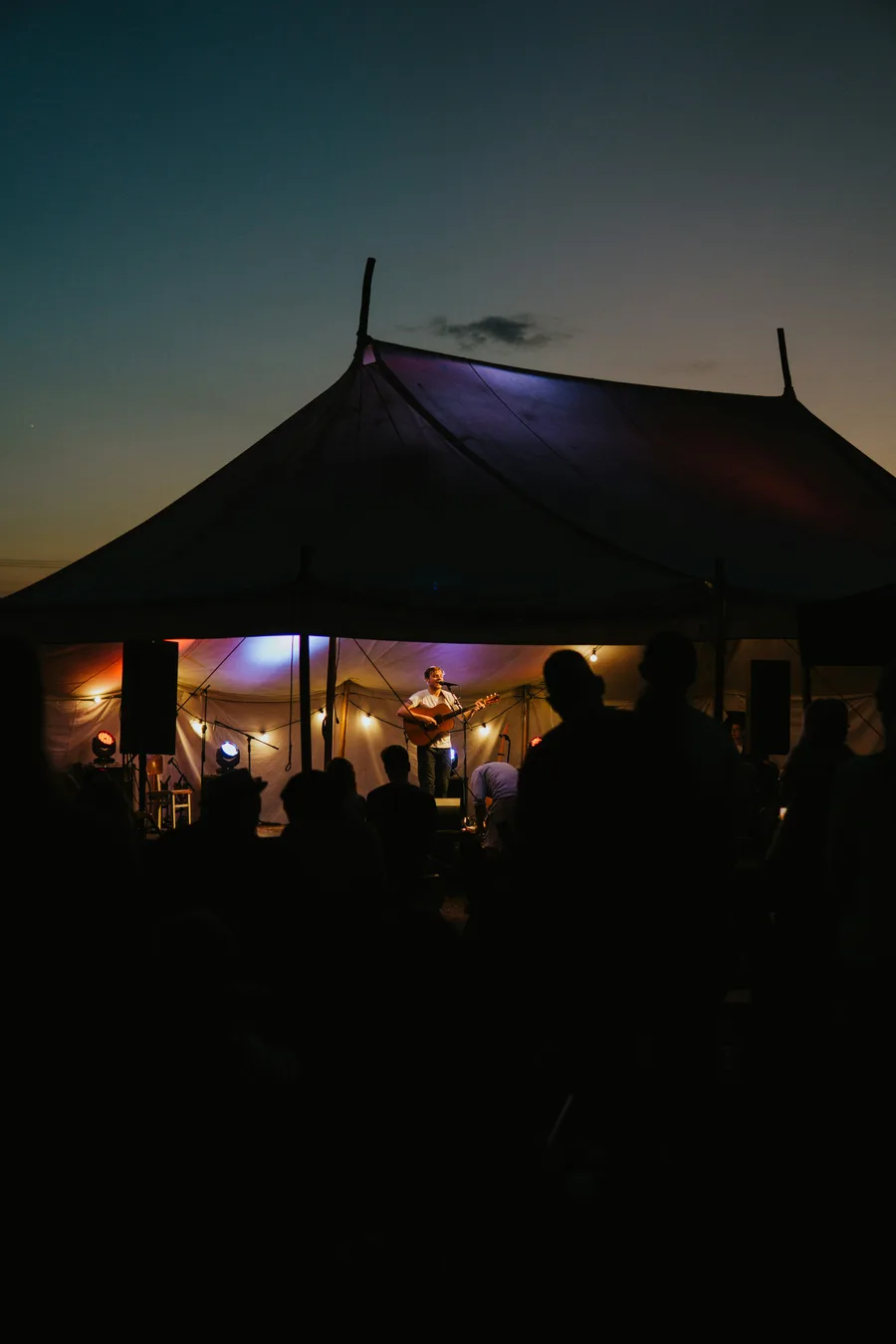 Sänger mit Akustikgitarre auf einer Festzeltbühne bei Nacht, Publikum im Vordergrund